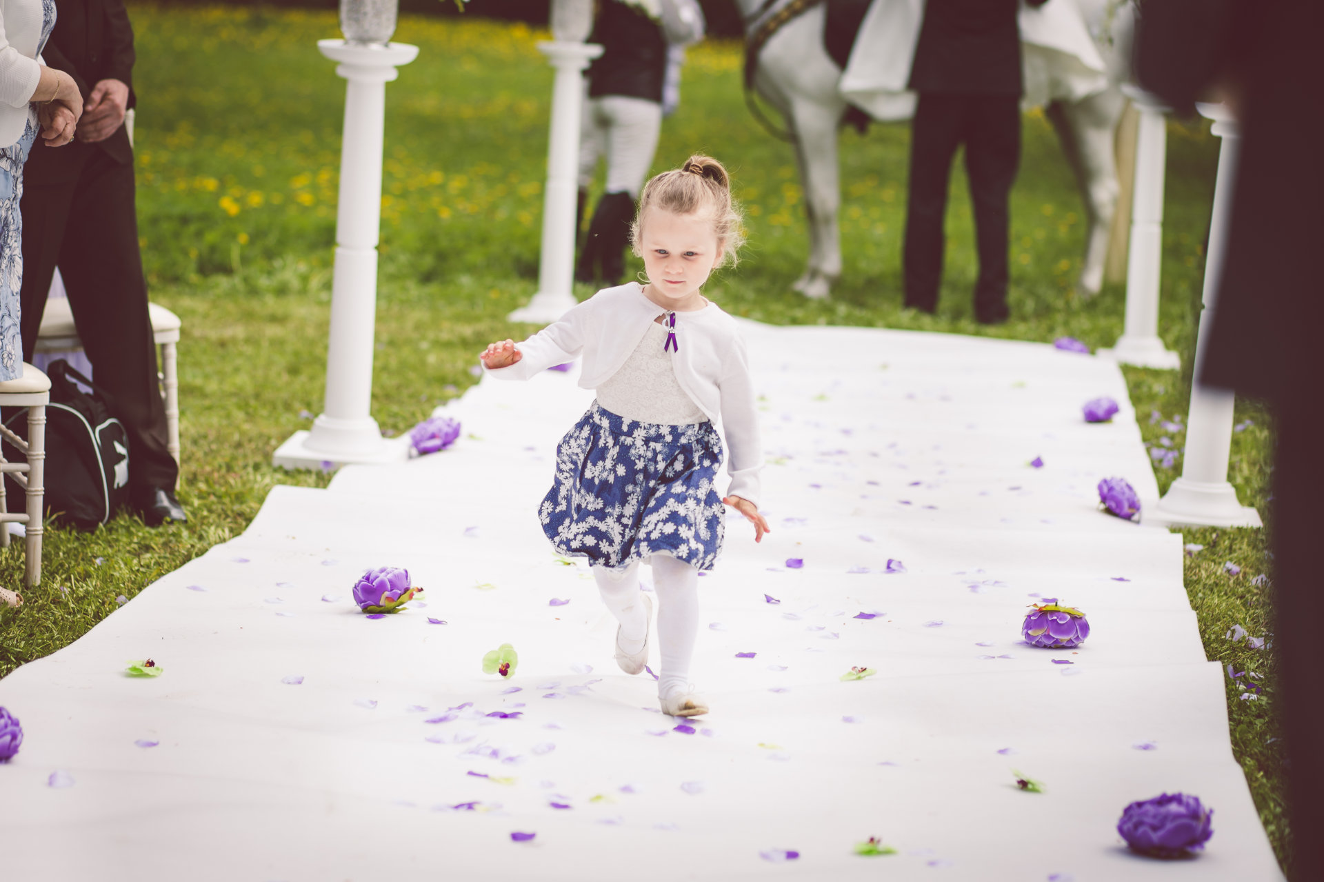 Dítě běžící po bílém svatebním koberci s květinami ke svatebnímu altánu